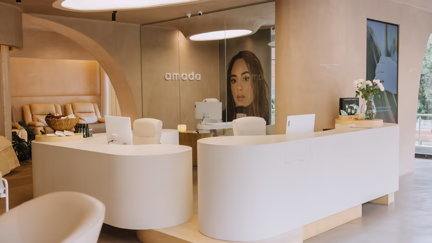 Recepción de Amada en Bogotá: mostrador curvo blanco, lucernarios ovalados y el logotipo de la marca sobre el muro