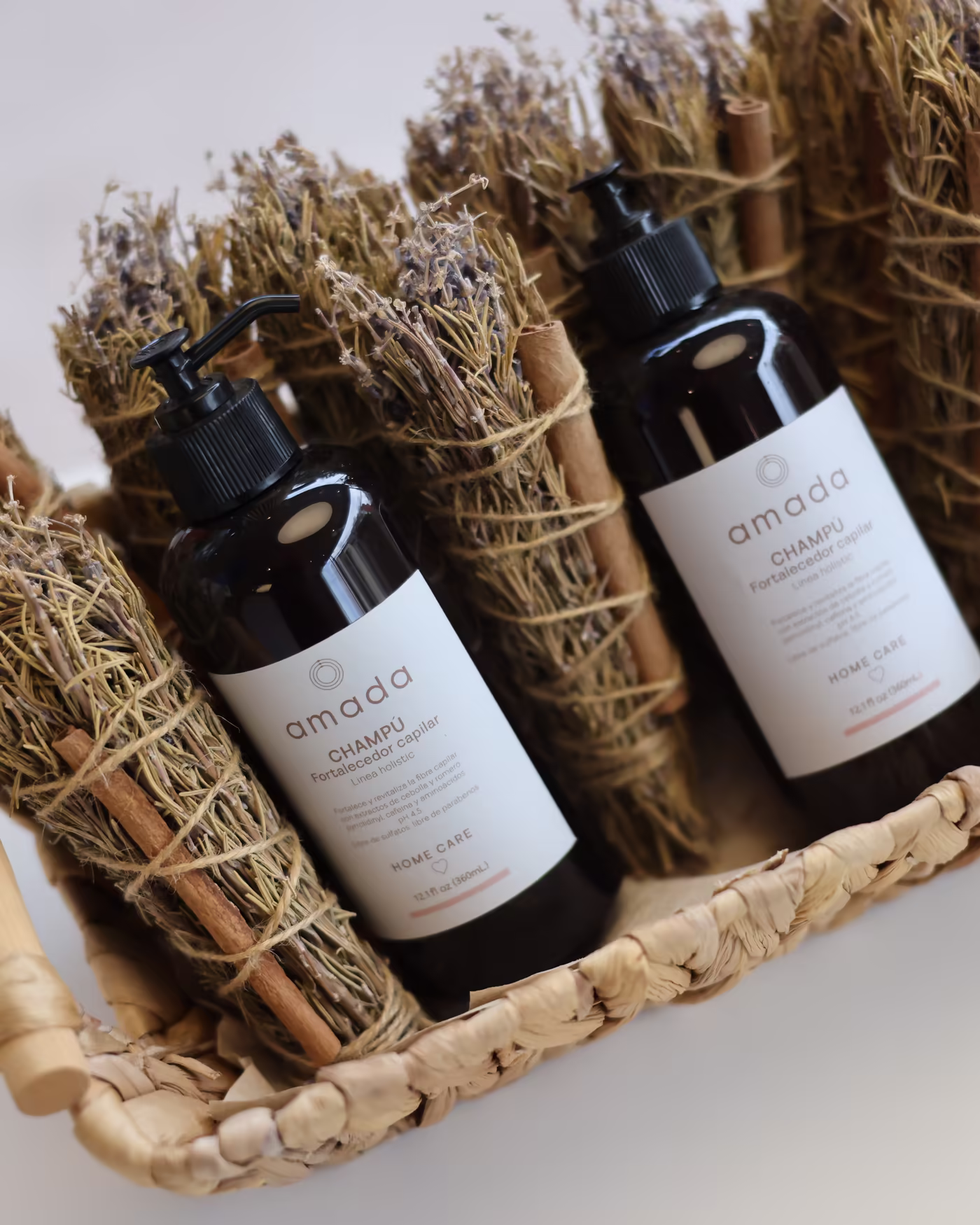Champú de la línea Amada en una canasta de mimbre entre atados de romero, lavanda y canela