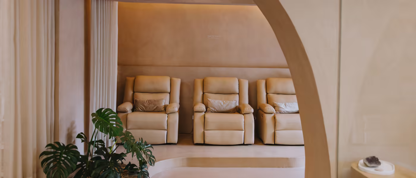 Sala de descanso de Amada vista a través de un arco: tres sillones reclinables, cortinas de lino y una monstera